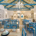 Interior del restaurante Beity Ibn Rushd en Córdoba con estilo árabe moderno, destacando sus sillas de madera azul, mesas preparadas y ambiente acogedor.