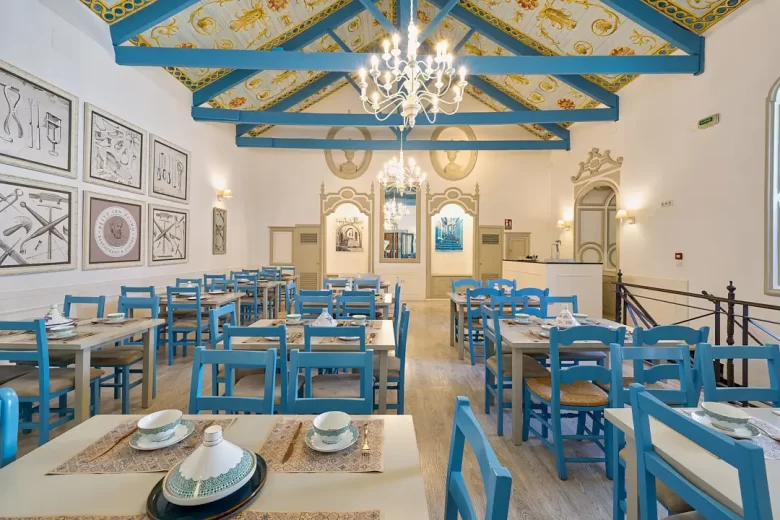 Interior del restaurante Beity Ibn Rushd en Córdoba con estilo árabe moderno, destacando sus sillas de madera azul, mesas preparadas y ambiente acogedor.